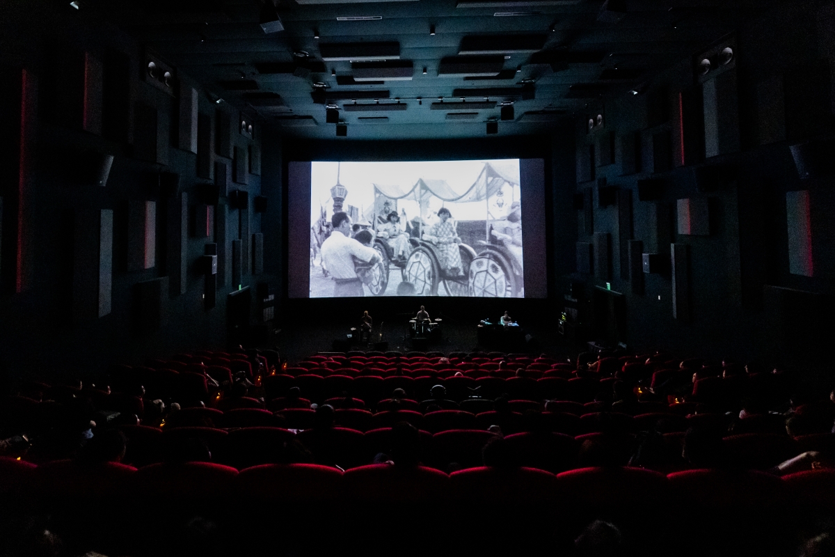 On a warm May evening, the opening ceremony of the 14th edition of the Taiwan International Documentary Festival (TIDF) was teeming with euphoria. Founded in 1998, TIDF takes seriously its motif of “re-encountering reality.” After two pandemic-hit iterations with online Q&As, this was the first time in six years that filmmakers and audiences had gathered in Taipei in person for the biennial festival. It was the second iteration to use the Taiwan Film and Audiovisual Institute’s (TFAI) beautiful new home in the Xinzhuang District, west of the Tamsui River, for many of the programmed events. The late iconic Taiwanese documentarian and image-maker Chang Chao-Tang made sure our brains emerged twisted and rewired from his two extraordinary opening shorts, which screened in TFAI’s new state-of-the-art cinema. In Homage to Chen Da (2000), one of the island’s greatest folk singers is filmed playing the two-stringed yueqin and singing an everyday history of modern, rural, and municipal Taiwan. Chen Da, a wandering bard, accompanies himself inside and outside his village home, by the river, and at the much-lamented Scarecrow Restaurant in Taipei (unaware of its premature demise 45 years ago, I tried to pay my own homage one day and found an ugly office building in its place). Chen Da has no accompanying dialogue or explanatory text, simply letting the singer unspool his oral histories of Taiwanese life. The sonic and social resonances with Malian guitar music, the Delta blues, and the Baul music from my part of the world provided more than enough context for everyone in the theater. If Chen Da was poignant, gentle, and melancholy, Chang’s second short was nothing less than revelatory; when it was first broadcast on television in 1979, The Boat Burning Festival revolutionized Taiwanese documentary. Shot for the Kuomintang-owned China Television Company by Chang and a young Christopher Doyle in Sucuo Village in Tainan, the film documents a biennial Taoist ritual in which villagers decorate a large boat with intricate designs and figures. In a fervid procession of dancing and chanting, they raise the sail and set fire to the boat in a frenzy of religious ecstasy. Rarely have I been as conscious of a film as a visceral audiovisual experience. Chang wipes all diegetic sound, scoring the entire film instead to the prog-rock strains of Mike Oldfield’s album Ommadawn (1975). The split between audio and video jars, but is eerily apt, atomizing the very grain of cinematic expression into its separate components. The soundtrack was originally used without licensing, so this may well have been the film’s first legal theatrical screening in Taiwanese history. The Irish folk instruments (and glockenspiel) that soak Ommadawn in its otherworldly sense of new-age whimsy reinforce the crazed visuals of the boat burning ritual, manipulating them into crescendos and tranquilizing them into catharsis. This surreal juxtaposition transforms what might have been the merely anthropologically exotic into a hallucinatory, at times minatory, 22-minute epic—an acid trip without the acid. The lights came on to rapturous applause and we exited in a daze of bliss. Various stills from “The Boat Burning Festival” highlighting the reactions of attendees to the chaos of the event. Stills from The Boat Burning Festival. Courtesy of TIDF. Earlier in the evening, Chang’s son accepted the Outstanding Contribution Award on his late father’s behalf. Chang, a TIDF co-founder who died in April this year, would have been thrilled at the reaction to his maverick avant-gardism—there were three screenings of his double bill at the festival, and they all sold out. At a time when the Great Powers have been attempting to manipulate Taiwanese sovereignty like a pawn on the geopolitical chessboard, TIDF has made an explicit effort to hew to its mandate of artistic autonomy. Four days after the festival, the Chinese military announced “punishment” drills all around the island as a show of force against “separatist acts.” Festival staff used the awards ceremony to connect political independence to documentary exhibition. “We have a free and democratic society,” TFAI chairperson Arthur Chu said pointedly, “so we can screen all kinds of films.” When “the world is complicated and full of conflict,” program director Wood Lin insisted on the need to preserve cultural memory: “We exist because of those who remember us. That is the power of documentaries.” To reconfigure our approach to historical memory and the relationships between oikos and polis, TIDF included special sections based, broadly speaking, on archival footage. “Untitled Reel” exhibited amateur and small-gauge films from TFAI holdings—home movies that have traditionally been excluded from film history, such as those by a doctor in pre–World War II Taiwan, or by the local photographer Hsu Tsang-tse in the sixties. There were talks on the history of 9.5- and 8mm reels in Taiwan, and a live cinema event, in which musicians were invited to perform synchronously to a screening of This Is Not a Film by Deng Nan-guang (Huang Pang-Chuan and Chunni Lin, 2023), itself stitched together from found small-gauge footage presumably shot by the renowned photographer Deng Nan-guang. In a similar vein, the “Appropriate Appropriation: Archive and More” program exhibited widely varying appropriated films that, in the words of TIDF programmer Chen Wanling, “liberate memories.” The standout film in this section was also the winner of the Special Prize in the Asian Vision Competition, Damnatio Memoriae (2023), by the oft-banned Thai filmmaker Thunska Pansittivorakul. A 109-minute montage of newsreels and propaganda clips from modern Southeast and East Asian history, the film is a jigsaw of repression and massacre, from the White Terror in post-1949 Taiwan to the execution of the Burmese politician and hip-hop artist Zayar Thaw in 2022. Warbling through the decades is the music and public persona of Teresa Teng, the Eternal Queen of Asian Pop, who in her short life became both a tool of propaganda and a referent for resistance in East and Southeast Asia. In the Audience Award–winning My Stolen Planet (dir. Farahnaz Sharifi, 2024), private records—old photos and videos of the filmmaker’s own family and friends, as well as 8mm footage shot decades ago by strangers and bought in the video stores of Tehran—are transformed into a mosaic of public memory. This slice of microhistory also won the Next Generation Award, organized in tandem with a local education program and decided by eighteen teenage jurors. The exercise endeavors to train future jurors and let younger people participate in a cultural practice that is too often a prerogative of age and experience. It is TIDF’s clearest expression of the direction it hopes to map for creative freedom in the region: forward. That direction is also significant for the Visionary Award, given to films that, as one juror told me, “chart a course forward, taking artistic risks along the way.” Both films chosen—The Clinic (dir. Midi Z, 2023) and Taman-taman (Park) (dir. So Yo-hen, 2024)—“were remarkable for all the ways they resisted classical interpretation, and instead depicted closed worlds operating under their own idiosyncratic rules.” Winner of the Special Jury Prize in the Visionary category, as well as the Grand Prize in the Taiwan Competition, Taman-taman is a quiet exercise in metanarrative. Two poets, both Indonesian immigrants, meet in Tainan Park to recite poetry, eavesdrop, invent, digress, and pretend to broadcast the gossip, anecdotes, tidbits, rumors, and short stories of migrant workers in Taiwan. Meditative and experimental and operating in a unique spatiotemporal continuum, the film is both moving and immobile. “It’s been going around in circles,” one of the protagonists complains at one point. “This film is getting more and more unclear.” On the other side of obscurity often lies epiphany. One evening, at the Taiwan Contemporary Culture Lab, a former military base that’s been converted into blocks of performance and lecture spaces, I experienced a singularly exhilarating event that converted confusion into fun. In “Jamming with Archive: Re-coding,” five groups of artists were let loose in what used to be an old mess hall for soldiers. With access to TFAI’s collection of 6,000-plus propaganda newsreels from the KMT-era Taiwan Film Culture Company, the artists performed acts of what the film scholar Jaimie Baron calls “archival ventriloquism”—reusing, misusing, and deconstructing these clips in real time to spark new sensations and discombobulate the spectatorial gaze. Using multiple sound consoles, open-source software, machine learning, and on-site sensing, and forcing the audience to keep changing places by turning toward different screens, erstwhile political assets were transformed into audiovisual art. “As the archives become digitized,” Wood Lin told me in the rapturous darkness, as windows of text vibrated into reels of political rallies to pulsing electronica, “propaganda becomes code.” For the finale, the artist duo YouNuts flashed black-and-white newsreels and released white balloons into the audience in an echo of the ones that used to be sent toward mainland China decades ago with supplies and propaganda. We started kicking and punching balloons at each other, playing with them like children. Inflating menacingly right in front of the screen, an enormous white balloon itself became a diaphanous, bulbous screen (till it finally exploded, almost perfectly in sync with everything going black). By the end, balloons were popping, and people were squealing with joy. A dark, crowded room with a screen showing a mans face. There are multiple balloons in front of the screen refracting the man's face. The audience sits and stands around the consoles managing the screening. TIDF event “Jamming with Archive: Re-coding”. Courtesy of TIDF. The C-Lab, as it’s commonly called, also played host to a masterclass by the Slovakian filmmaker Peter Kerekes, four of whose films were screened out of competition. His latest, 107 Mothers (2021), falls somewhere between documentary and fiction, “a bastard,” as he described it. The docudrama is populated by a mix of Ukrainian actors and real prisoners of Prison 74 in Odessa, where the children of female convicts are allowed to be with their mothers till their third birthday. Kerekes told me about an “interesting paradox,” wherein the scaffolding of fiction let more reality in: “All the guards tried to make the prison look nicer when we were filming it like a documentary. But ‘fiction’ helped me make a more realistic film about prisons.” Kerekes’s sardonic Cooking History (2009), an alternate (culinary) history of modern warfare, explores the role of military cooks in various 20th-century European conflicts. Rolling out to its logical extreme the old adage about an army marching on its stomach, the film poses an intriguing question to people who do not think of themselves as killers, from SS line cooks and Tito’s personal chef to the Frenchmen who fed the soldiers who killed Algerian rebels: if army cooks stopped cooking, might war disappear? Disappearances of a more historically concrete sort were the subject, in its Asian premiere, of the Grand Prize–winning The Trial (dir. Ulises de la Orden, 2023), an archival film that is as relevant today as when the source material was recorded in a Buenos Aires courtroom in 1985. Relatives and compañeros of dozens of those “disappeared” during the Dirty War give chilling testimony against the commanders of the military dictatorship that ruled Argentina between 1976 and 1983. Masterfully edited into a harrowing document of the Trial of the Juntas from over 500 hours of U-matic television footage that was never properly broadcast, The Trial made for severely uncomfortable, utterly gripping, and somewhat cathartic viewing. For three hours, I heard everyone around me sobbing. They probably heard me too. The biological need to remember trauma was a feature of much of the programming. In Sofía Paoli Thorne’s tactually sensuous Guapo’y (2023), Celsa Ramirez Rodas, an artist who was imprisoned 40 years ago by the Paraguayan secret police, strews rosemary to remember her cellmates (“They say it’s good for memory”) and puts herb poultices on her body to ease the pain of torture. Like many of the women in 107 Mothers or The Trial, Ramírez Rodas also gave birth in prison, and memories of dictatorships are recalled and relived on the body. There were memories, too, of catastrophe (Bye Bye Tiberias, dir. Lina Soualem, 2023) and lost childhoods (Kix, dir. Dávid Mikulán and Bálint Révész, 2024), and remarkable anthropologies of (neo)colonialism (Canuto’s Transformation, dir. Ernesto de Carvalho and Ariel Kuaray Ortega, 2023; Crossing Voices, dir. Raphaël Grisey and Bouba Touré, 2022; Where Zebus Speak French, dir. Nantenaina Lova, 2023). Some filmmakers answered postscreening questions in keffiyehs. One night, over taro and tapioca balls on shaved ice, folks from the Taipei Documentary Filmmakers’ Union urged festival guests to support unions. New memories were made in public parks around Linsen North Road, the old dormitory area for colonial-era Japanese soldiers. Near festival venues flanking Taipei’s red-light district, filmmakers would collapse on grassy knolls in 4:00 a.m. conversations with convenience-store cocktails (many mixed admirably by the Armenian filmmaker Silva Khnkanosian, a former bartender whose Far From Michigan [2023], filmed in bomb shelters in Nagorno-Karabakh, screened in competition). “All things considered,” juror Joost Daamen, senior programmer at IDFA, told me with a wistful smile as he left for the airport, “this comes close to being the perfect festival.”